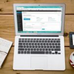 Turned-on Macbook Air Beside Black Iphone 4, Cup of Tea, and Notebook on Brown Wooden Surface