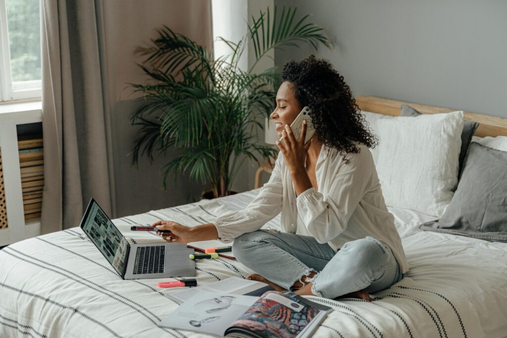 Woman in White Long Sleeve Using a Laptop while Having a Phone Call