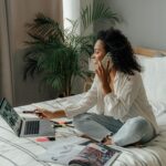 Woman in White Long Sleeve Using a Laptop while Having a Phone Call